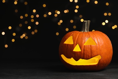 Photo of Pumpkin jack o'lantern on table against blurred background, space for text. Halloween decor
