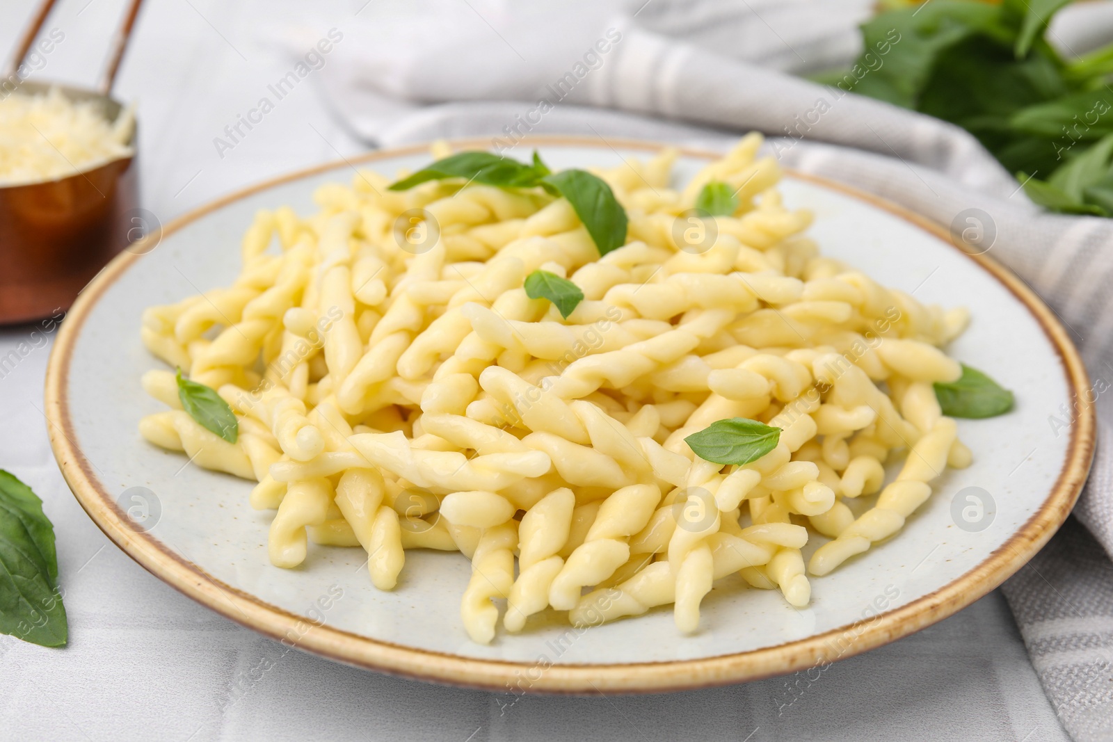 Photo of Plate of delicious trofie pasta with basil leaves on white tiled table