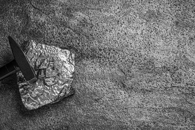 Photo of Pile of silver nuggets and hammer on grey textured table, top view. Space for text