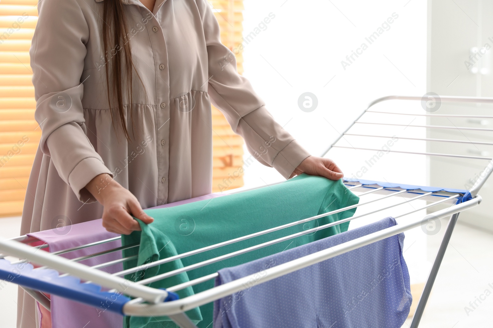 Photo of Young woman hanging clean laundry on drying rack at home, closeup