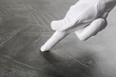 Photo of Person in white glove checking cleanliness of grey stone table, closeup