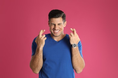Photo of Man with crossed fingers on pink background. Superstition concept