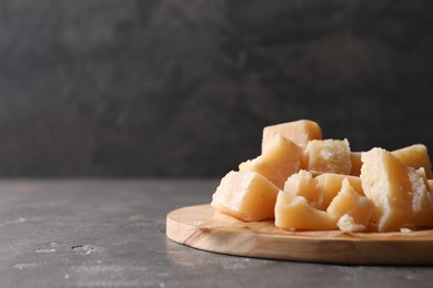 Photo of Parmesan cheese with wooden board on grey table. Space for text