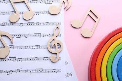 Photo of Baby songs. Music sheets, wooden notes and toy rainbow on pink background, flat lay