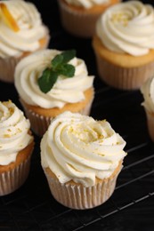 Photo of Delicious cupcakes with white cream and lemon zest on cooling rack, closeup