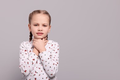 Girl suffering from sore throat on light grey background. Space for text