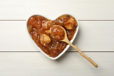 Photo of Tasty apple jam and spoon in heart shaped bowl on white wooden table, top view