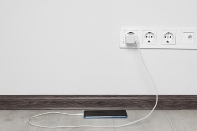 Photo of Modern smartphone charging from electric socket indoors. Space for text