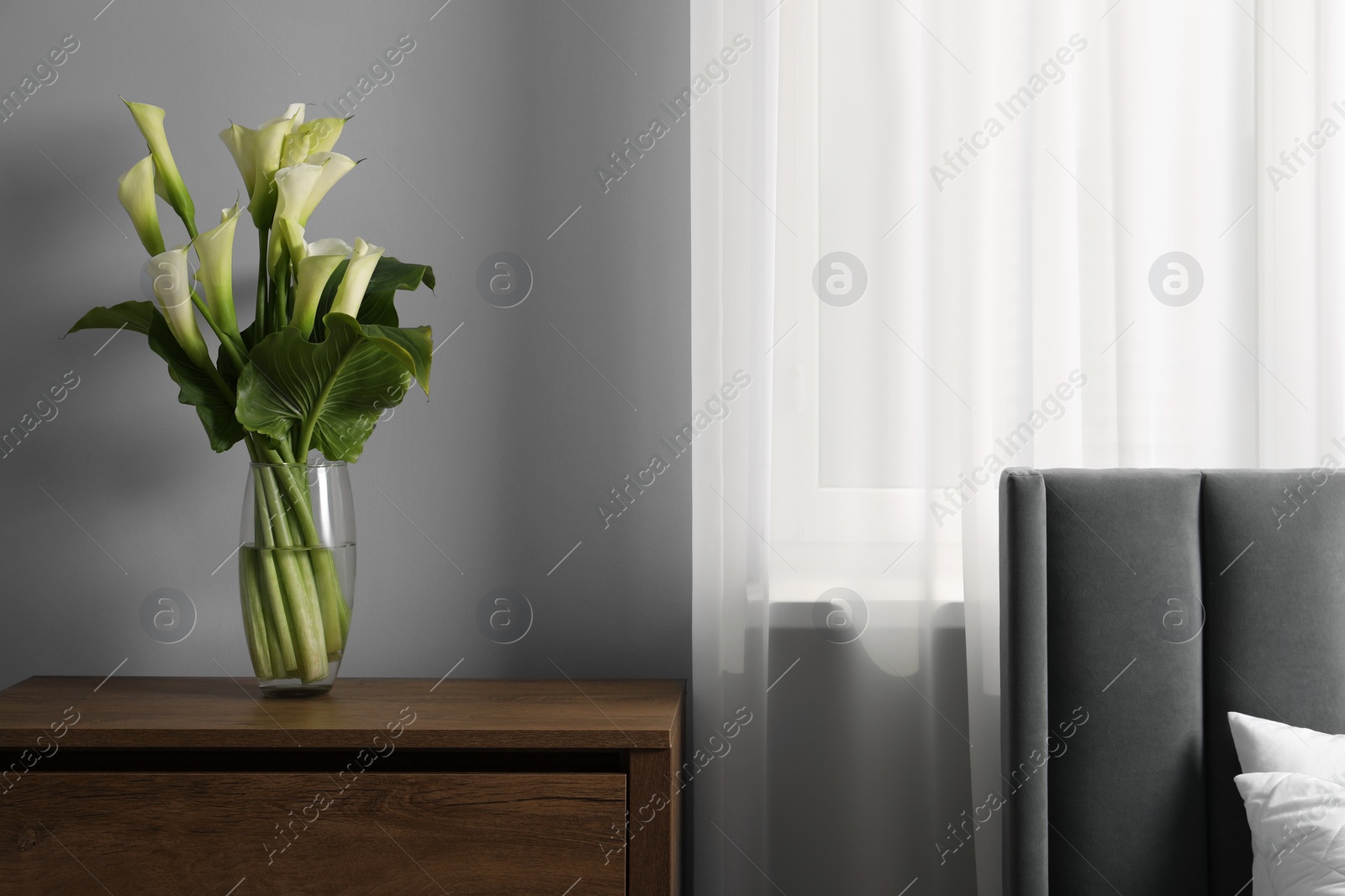 Photo of Beautiful calla lily flowers in vase on wooden bedside table