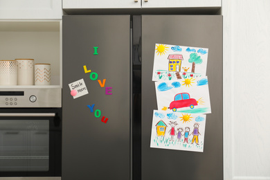 Photo of Modern refrigerator with child's drawings, note and magnets in kitchen