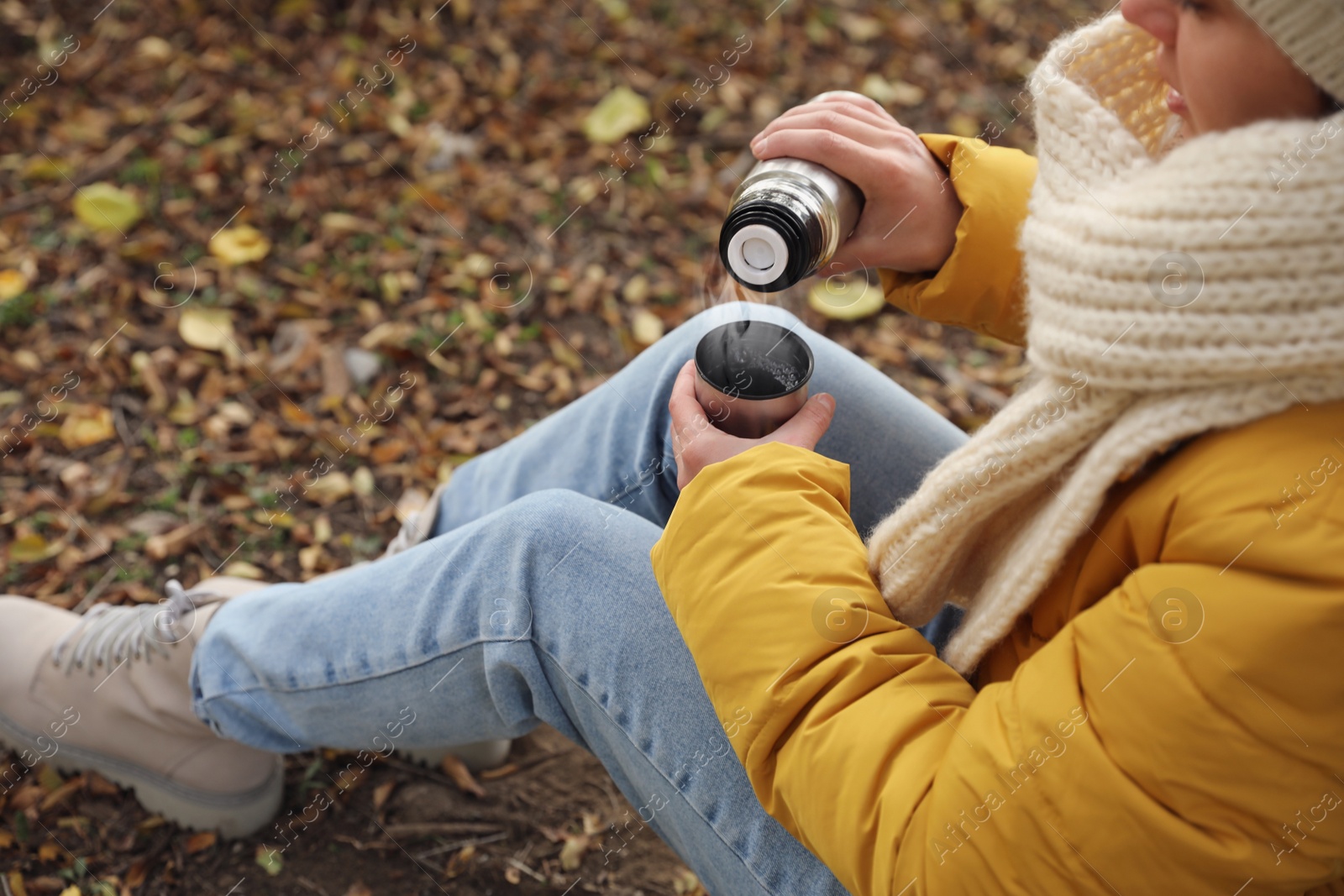 Photo of Woman with thermos sitting on ground outdoors, closeup
