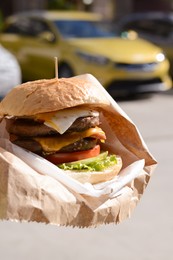 Photo of Delicious burger in paper wrap on city street, closeup