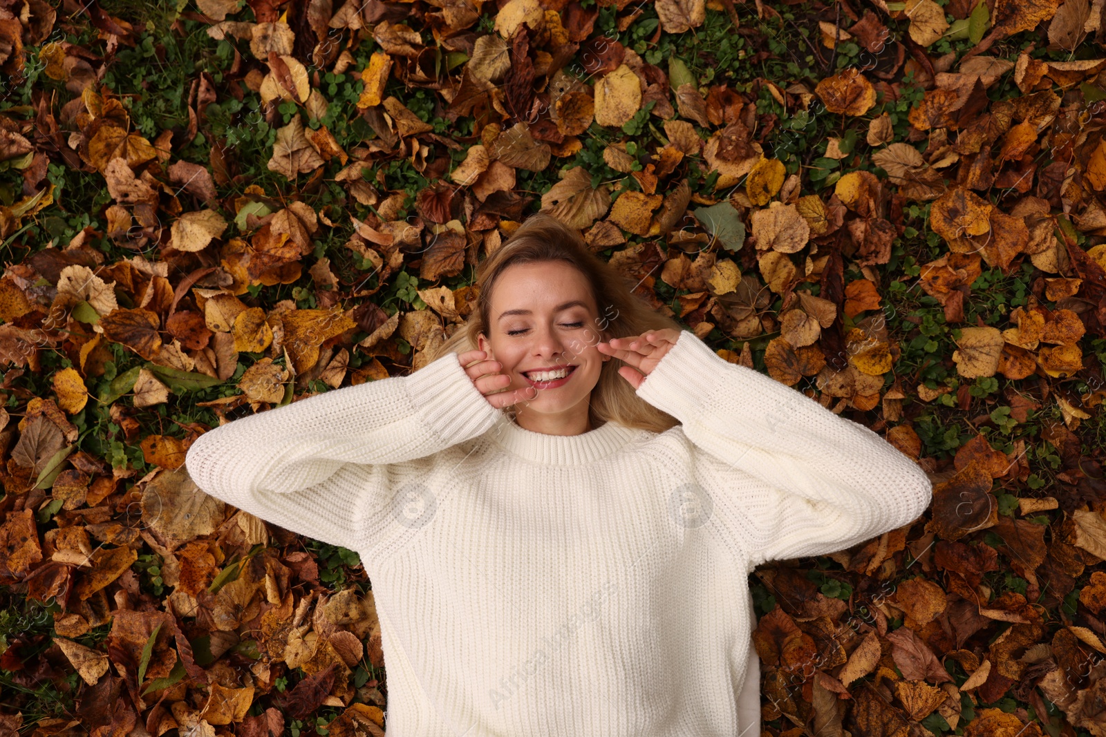 Photo of Smiling woman lying among autumn leaves outdoors, top view