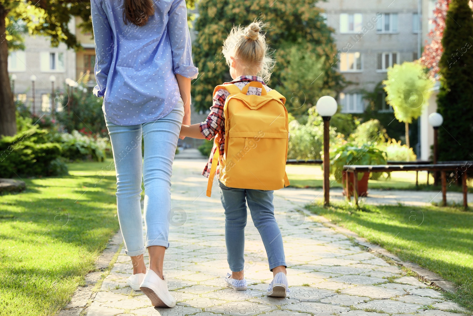 Photo of Young mother taking her little child to school through park