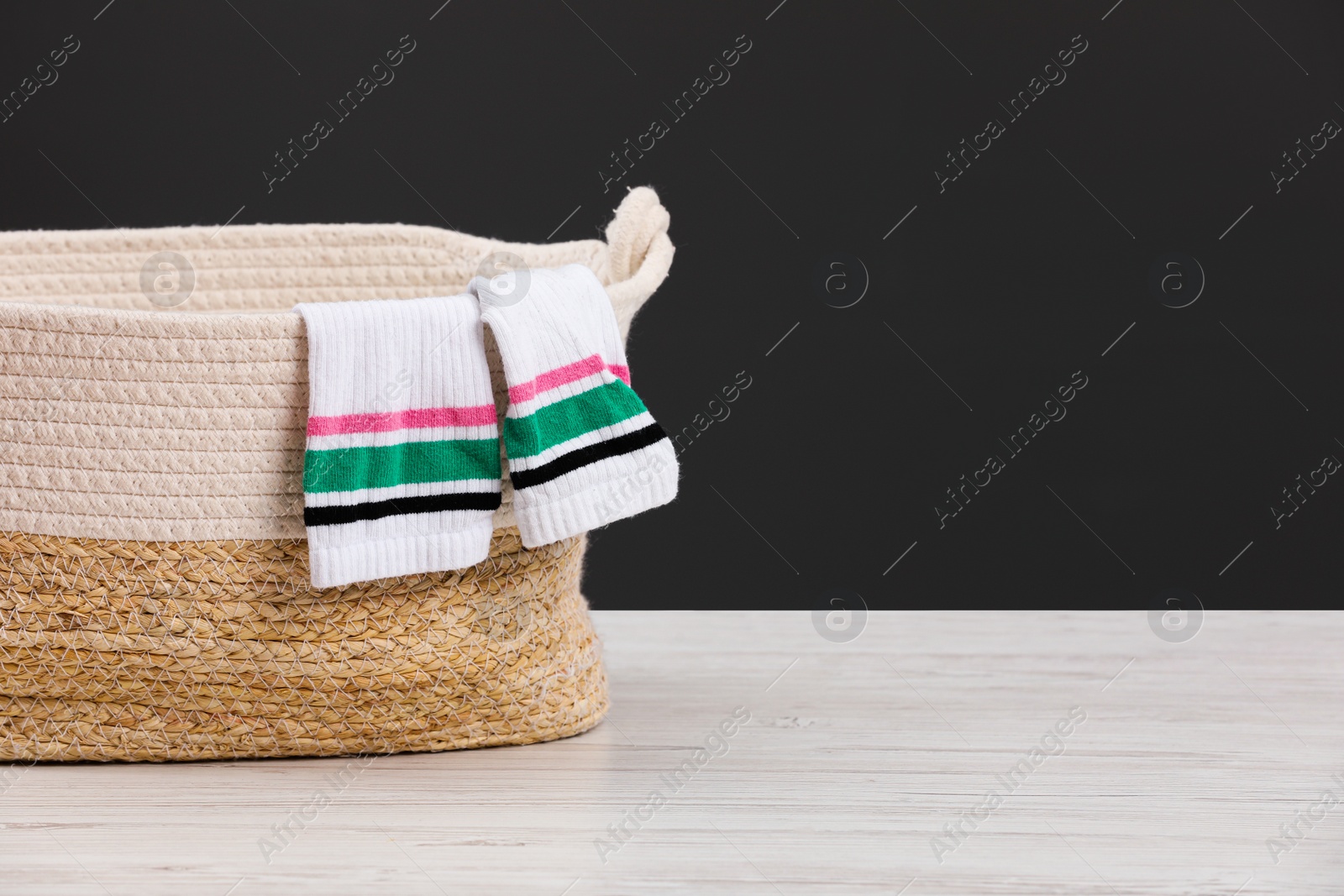 Photo of Wicker laundry basket with clothes near dark grey wall. Space for text