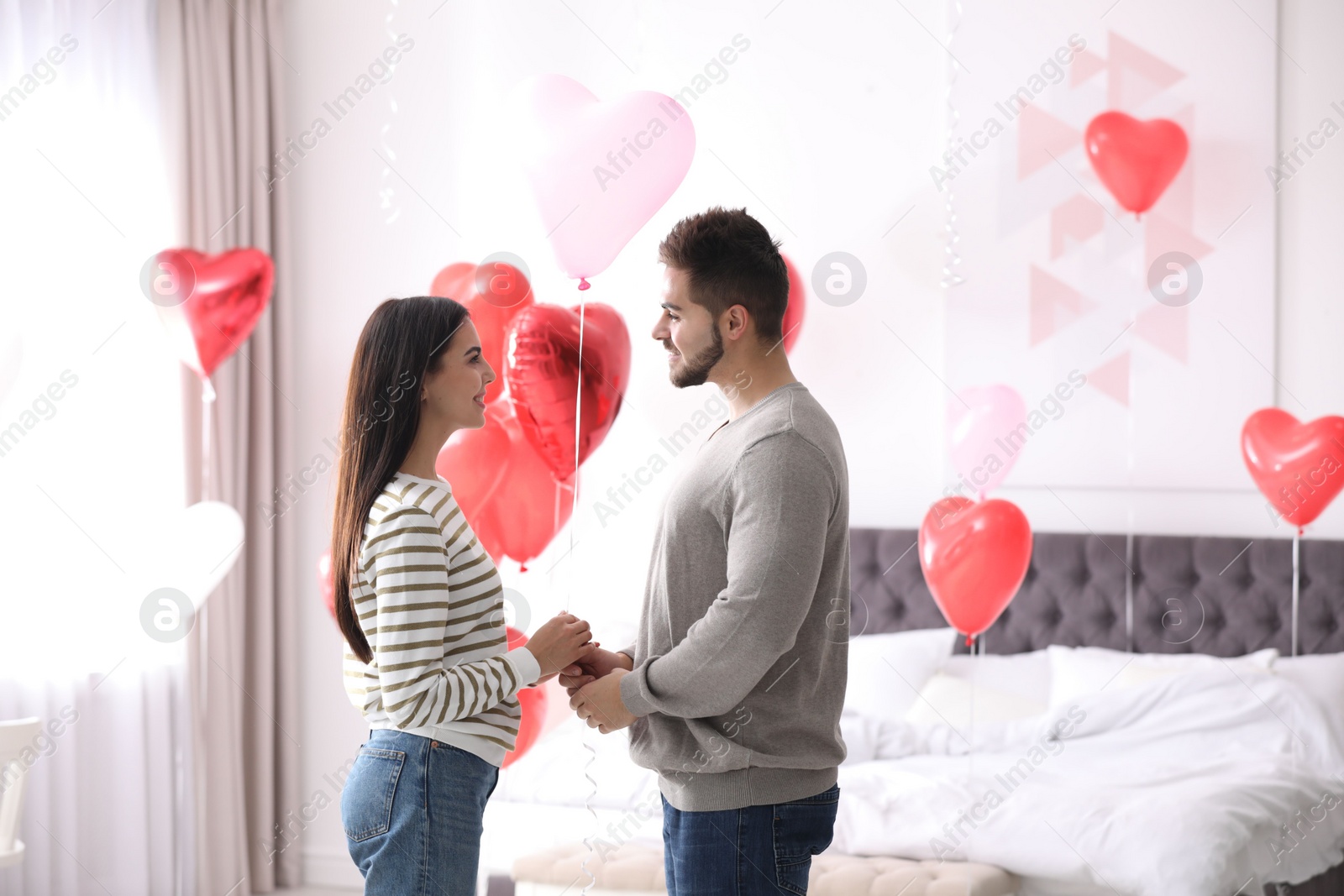 Photo of Lovely young couple in bedroom decorated with heart shaped balloons. Valentine's day celebration