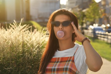 Photo of Beautiful woman blowing gum outdoors, space for text