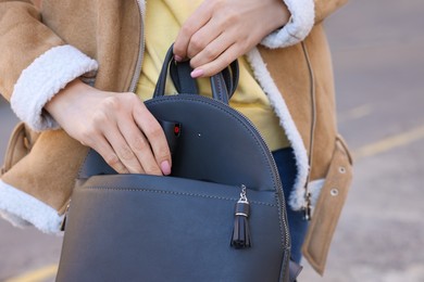 Photo of Young woman putting pepper spray into bag outdoors, closeup