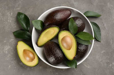 Whole and cut avocados on grey table, flat lay