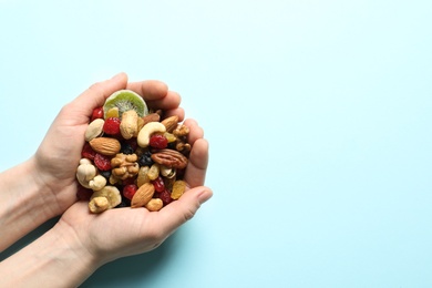 Woman holding handful of different dried fruits and nuts on color background, top view. Space for text