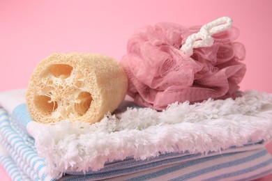 Shower puff, loofah sponge and towel on pink background, closeup