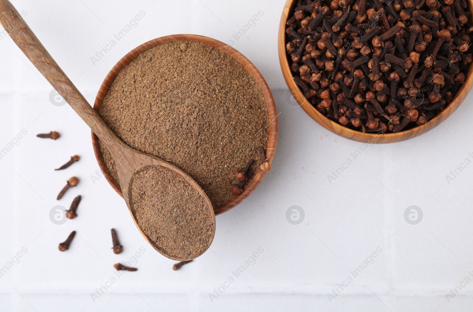 Photo of Aromatic clove powder and dried buds on white tiled table, top view