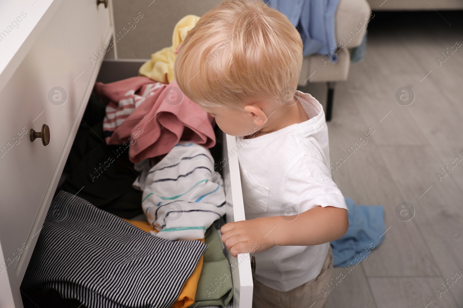 Photo of Cute little boy playing with clothes in dresser's drawer at home