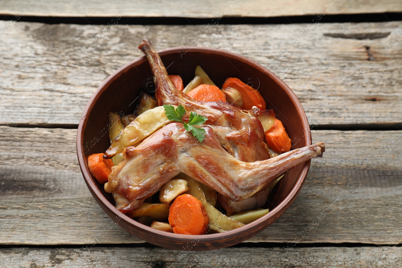 Photo of Tasty cooked rabbit with vegetables in bowl on wooden table