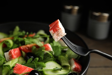 Photo of Closeup view of delicious crab stick salad in black bowl, focus on fork