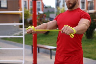 Photo of Muscular man doing exercise with elastic resistance band outdoors, closeup