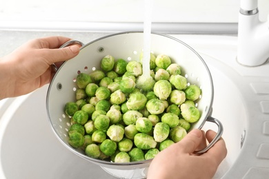 Woman washing fresh Brussels sprouts in colander, closeup