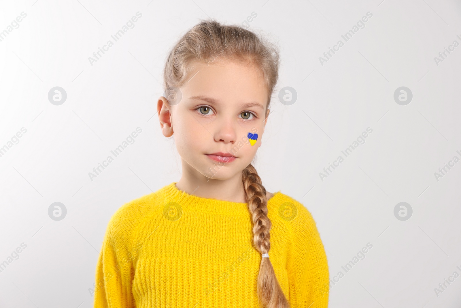 Photo of Little girl with drawing of Ukrainian flag on face against white background