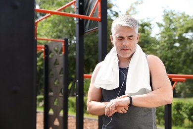 Handsome mature man looking at fitness tracker on sports ground, space for text. Healthy lifestyle