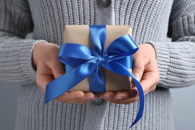Photo of Woman holding gift box with blue bow on light grey background, closeup