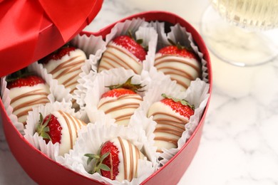 Heart shaped box with delicious chocolate covered strawberries on white marble table, closeup