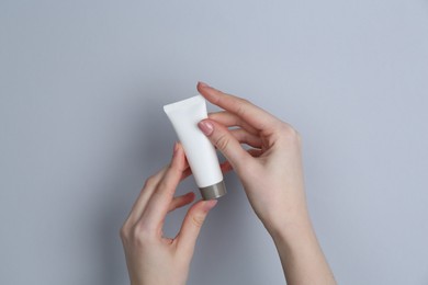 Photo of Woman holding tube of cream on grey background, closeup