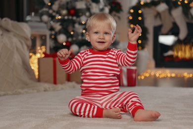 Cute baby in bright pajamas sitting near Christmas tree at home