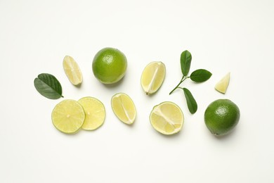 Photo of Whole and cut fresh ripe limes with green leaves on white background, flat lay