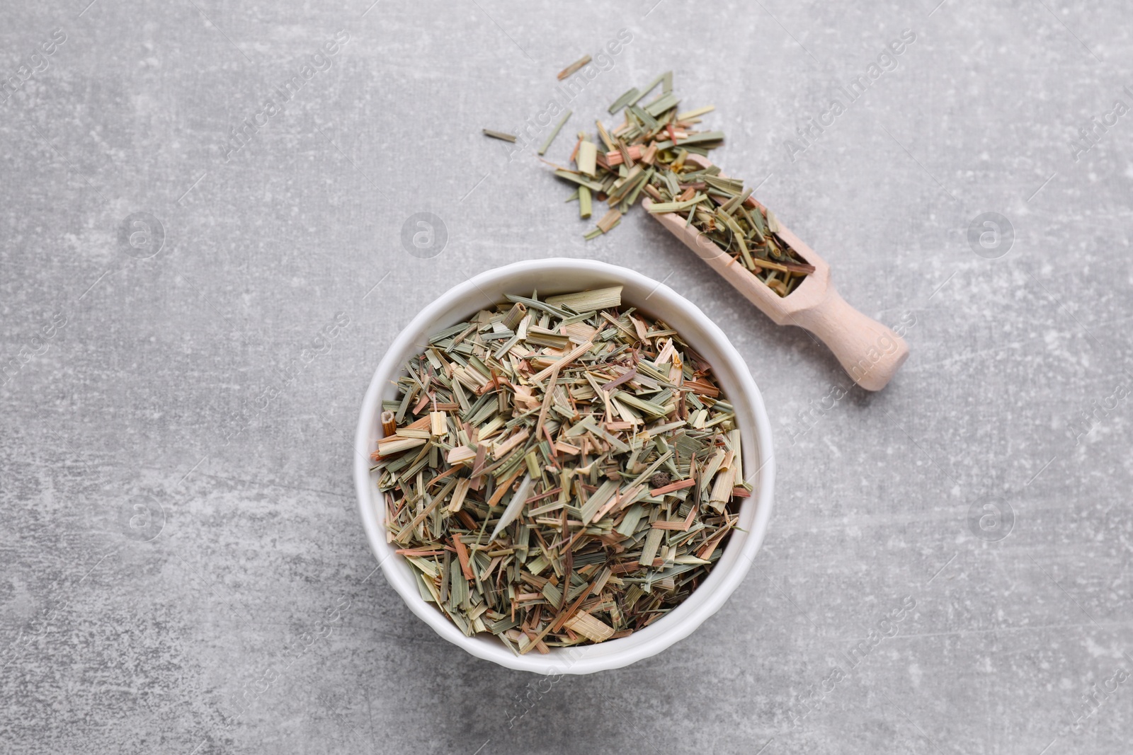 Photo of Bowl and scoop with aromatic dried lemongrass on light grey table, flat lay