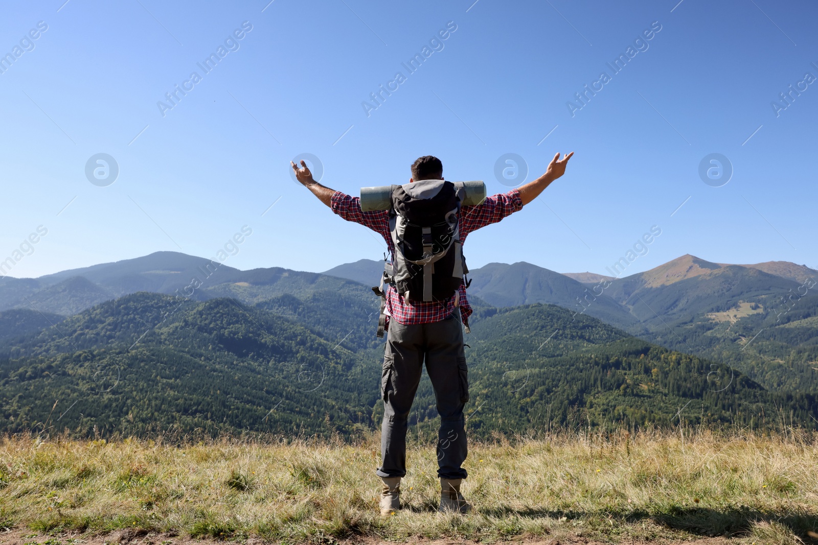 Photo of Happy man with backpack and camping mat in mountains on sunny day, back view