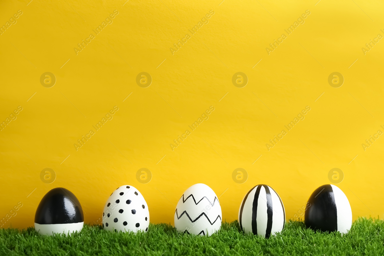 Photo of Line of painted Easter eggs on green lawn against color background, space for text