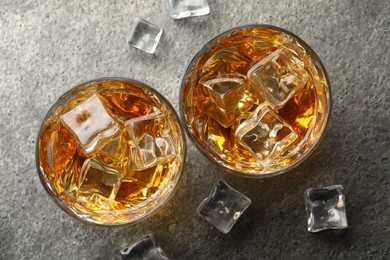 Photo of Whiskey and ice cubes in glasses on grey textured table, top view