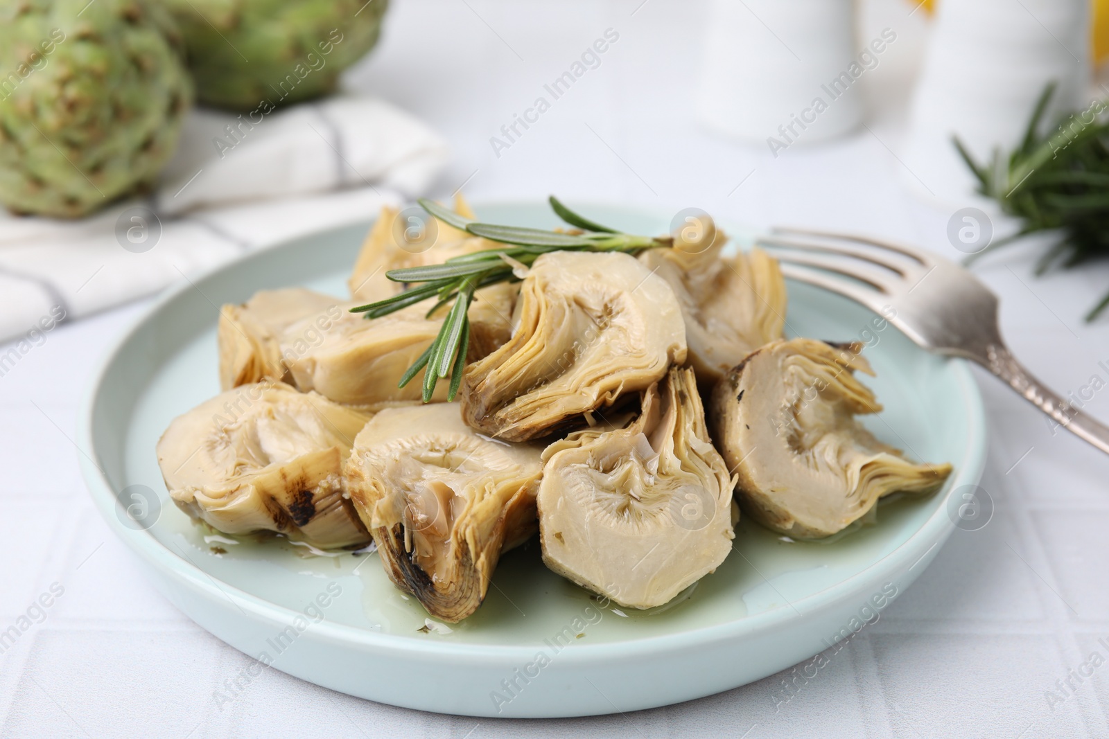 Photo of Plate with pickled artichokes and rosemary on white tiled table, closeup