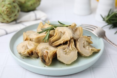 Photo of Plate with pickled artichokes and rosemary on white tiled table, closeup