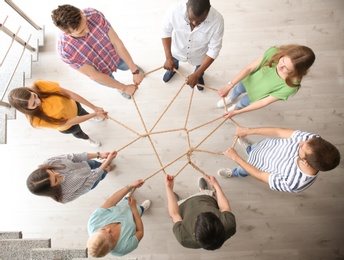 Photo of People holding rope together indoors, top view. Unity concept