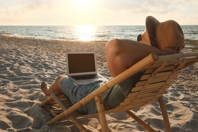 Man with laptop relaxing in deck chair on beach