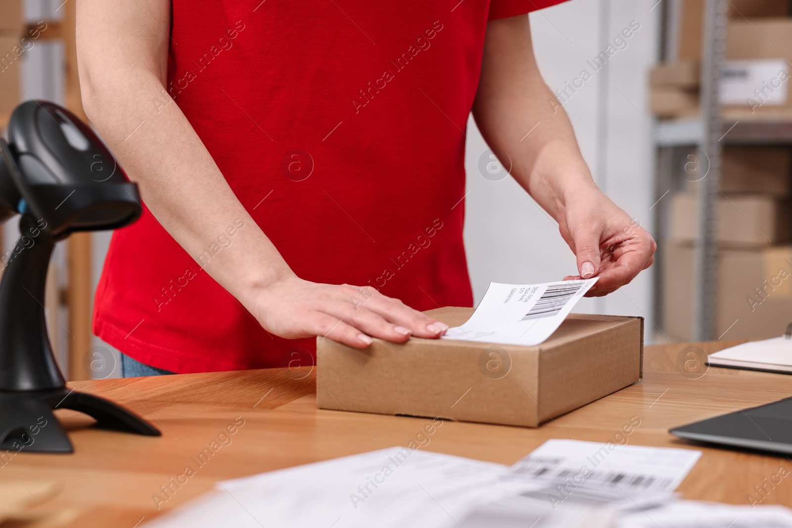 Photo of Parcel packing. Post office worker sticking barcode on box at wooden table indoors, closeup