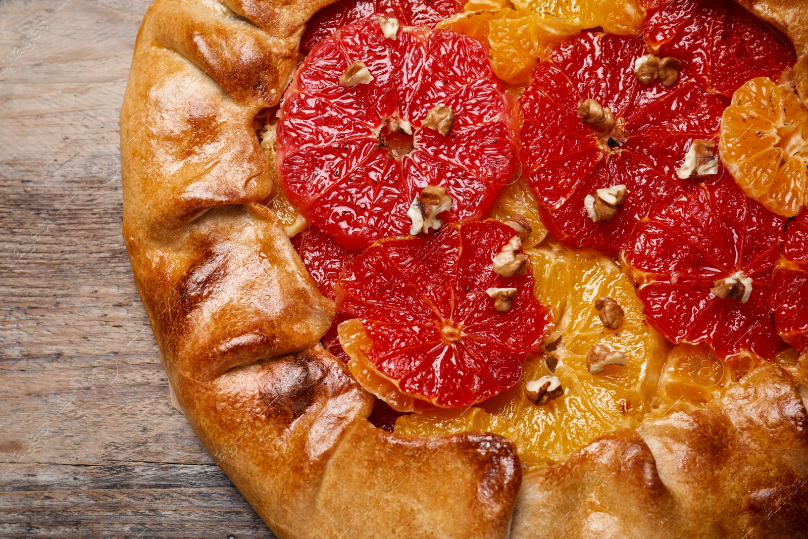 Photo of Delicious galette with citrus fruits and walnuts on wooden table, top view