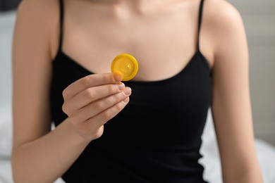 Photo of Woman holding unpacked condom on blurred background, closeup. Safe sex
