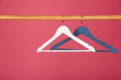 Photo of Empty clothes hangers on wooden rail against color background